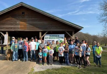 A group of volunteers posing in front of a building with a banner that reads 'Volunteer to Keep Arkansas Beautiful'.