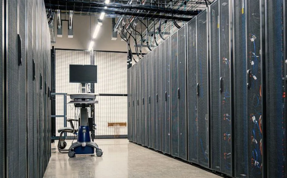 A large server room with rows of tall, gray servers and a small, wheeled workstation in the center.